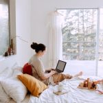 adorable toddler girl playing with wooden blocks sitting on bed while mother using laptop on sunny morning